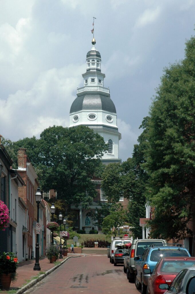 A narrow brick-sidewalk street lined with row houses leading up to the white State House dome