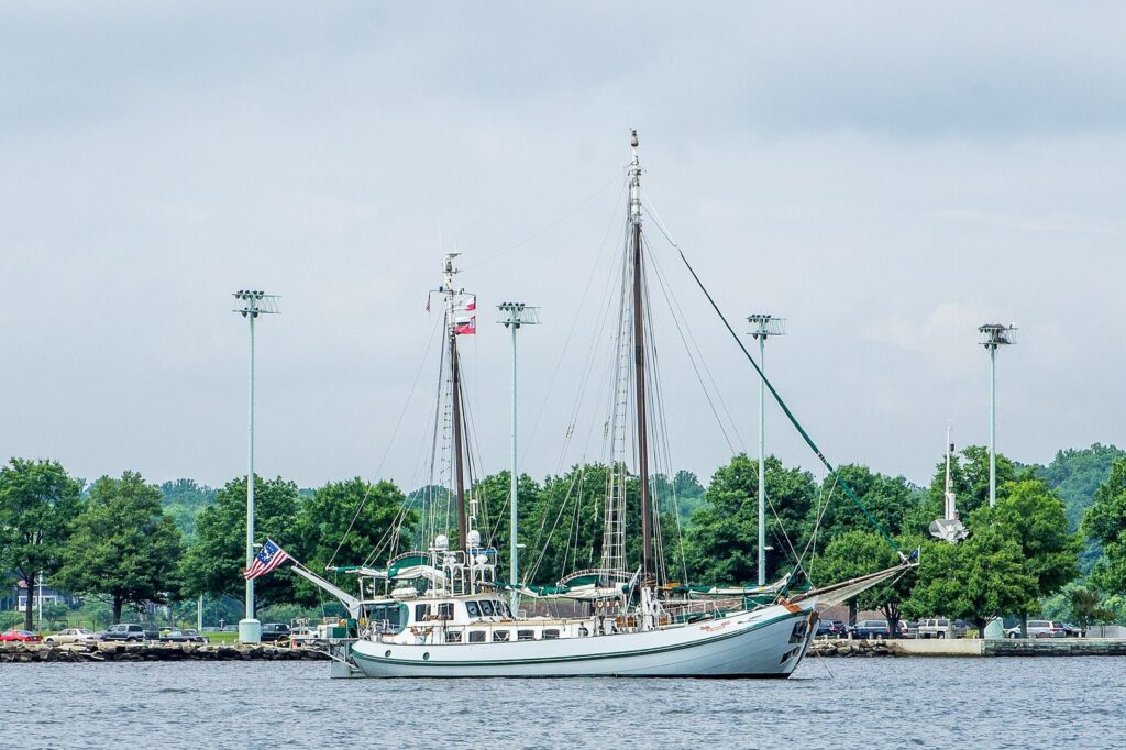A two-masted schooner at anchor in the harbor with a green shoreline behind