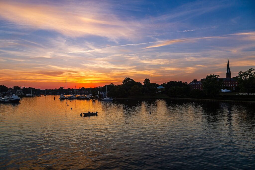 An orange and purple sunset over Spa Creek with moored boats and a church steeple silhouetted on the shore