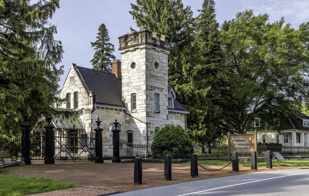 The stone lodge and iron gates at the entrance to Antietam National Cemetery under tall evergreens