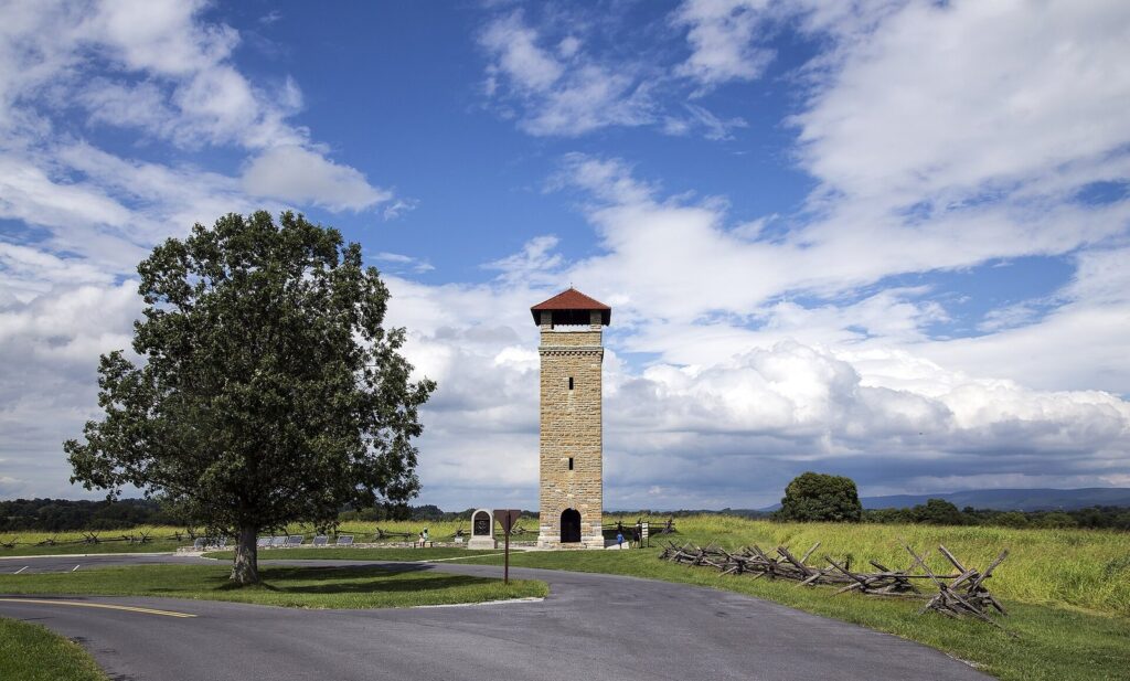 The stone observation tower with a red roof beside a big tree and a curving tour road over the battlefield