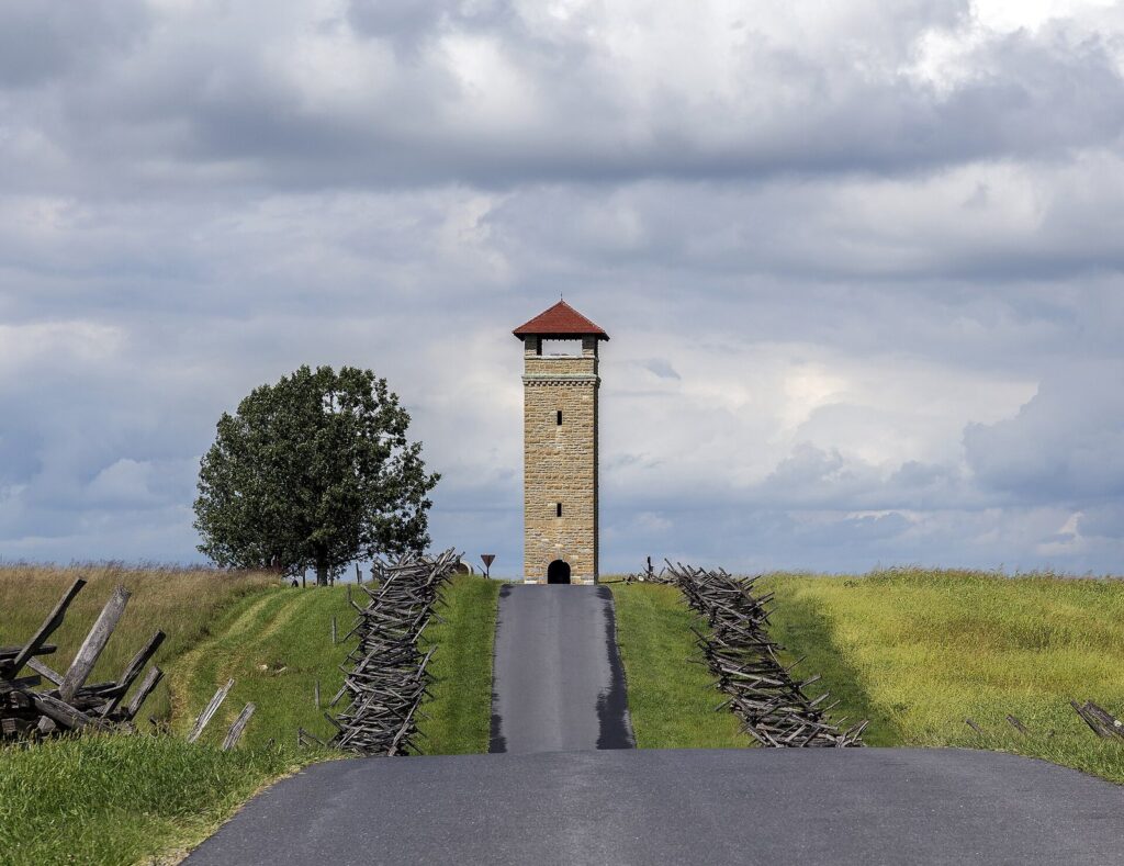 A stone observation tower at the end of a paved lane between split-rail fences