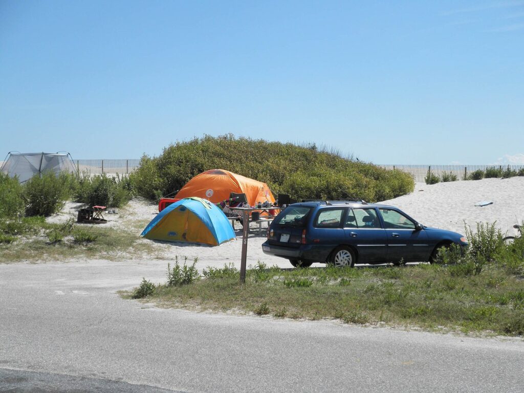 Tents and a station wagon at a sandy campsite tucked behind the dunes