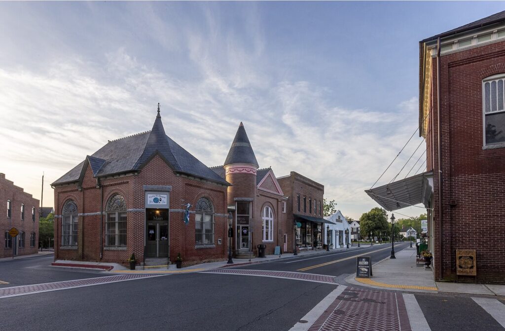 Brick storefronts and a turreted Victorian building at a Main Street intersection in Berlin, Maryland