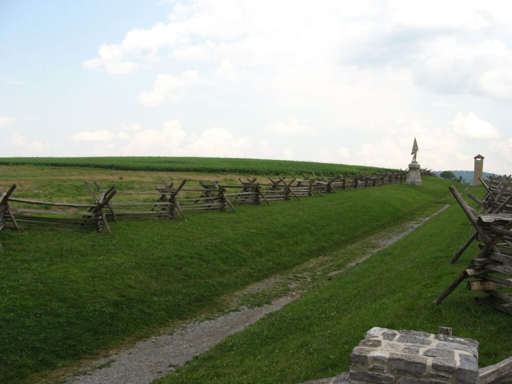 The grassy Sunken Road at Antietam lined by a zigzag rail fence, with the stone observation tower in the distance