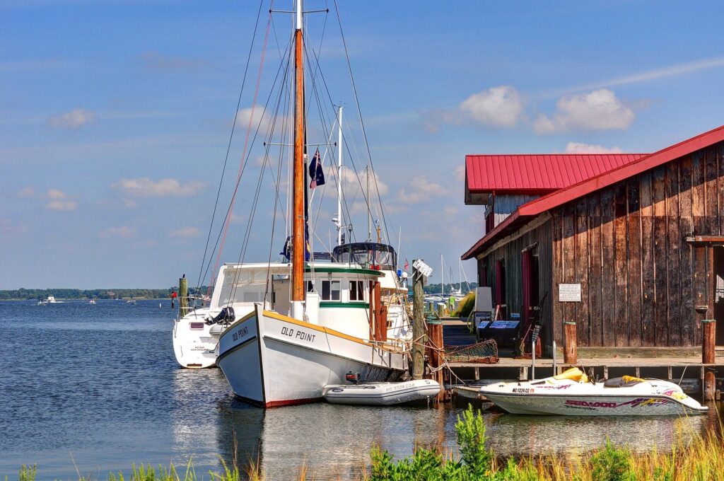 A white wooden workboat moored at a dock beside a weathered building with a red roof, the river behind
