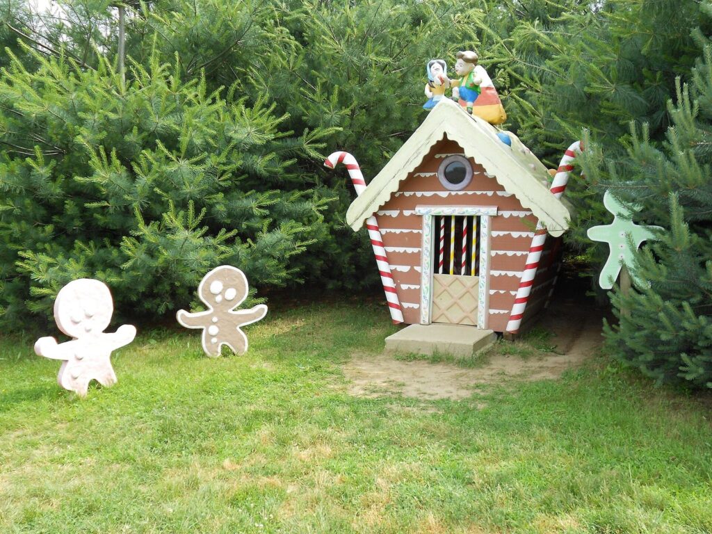 A small gingerbread house with candy-cane posts and cutout gingerbread men on the grass at Clark's Elioak Farm