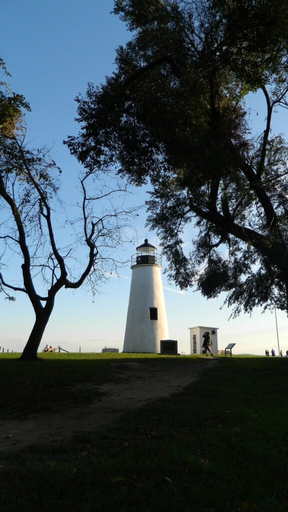 A white stone lighthouse framed by trees at the end of a grassy point