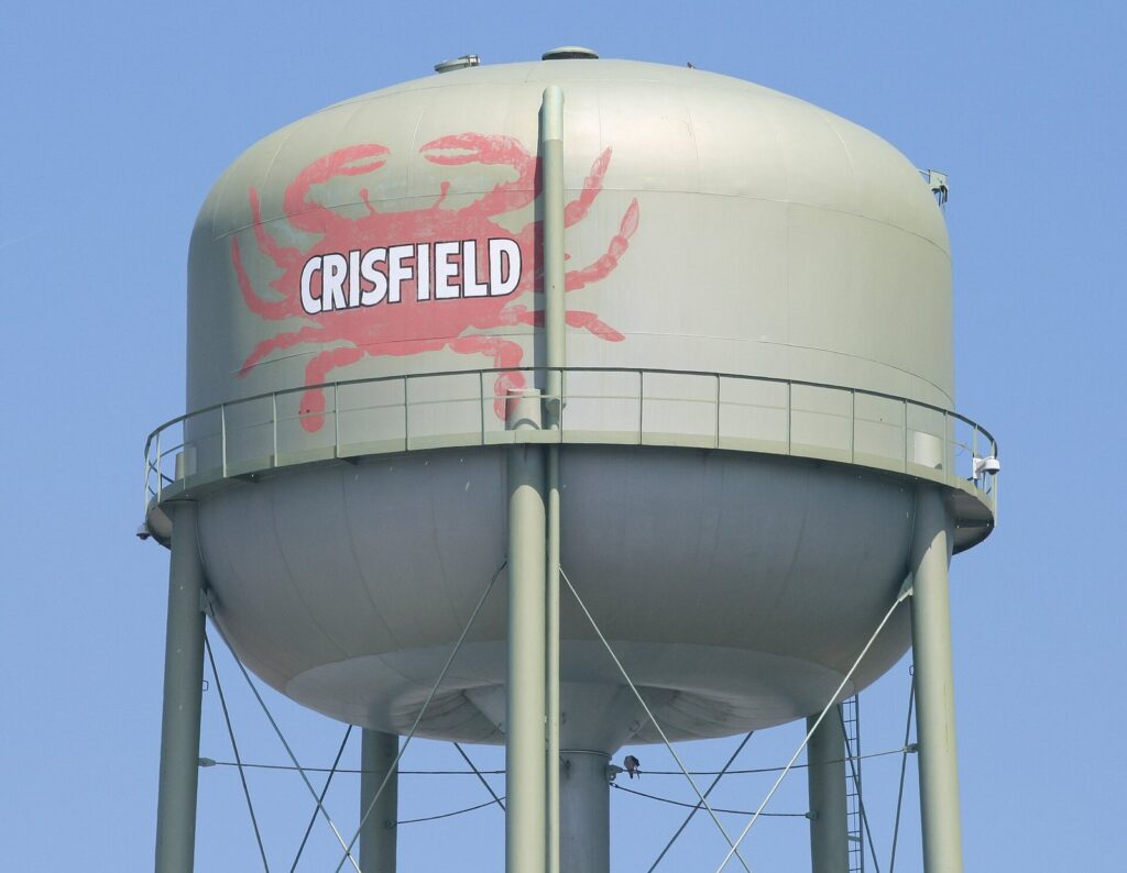 A pale green water tower painted with a large red crab and the word Crisfield against a blue sky