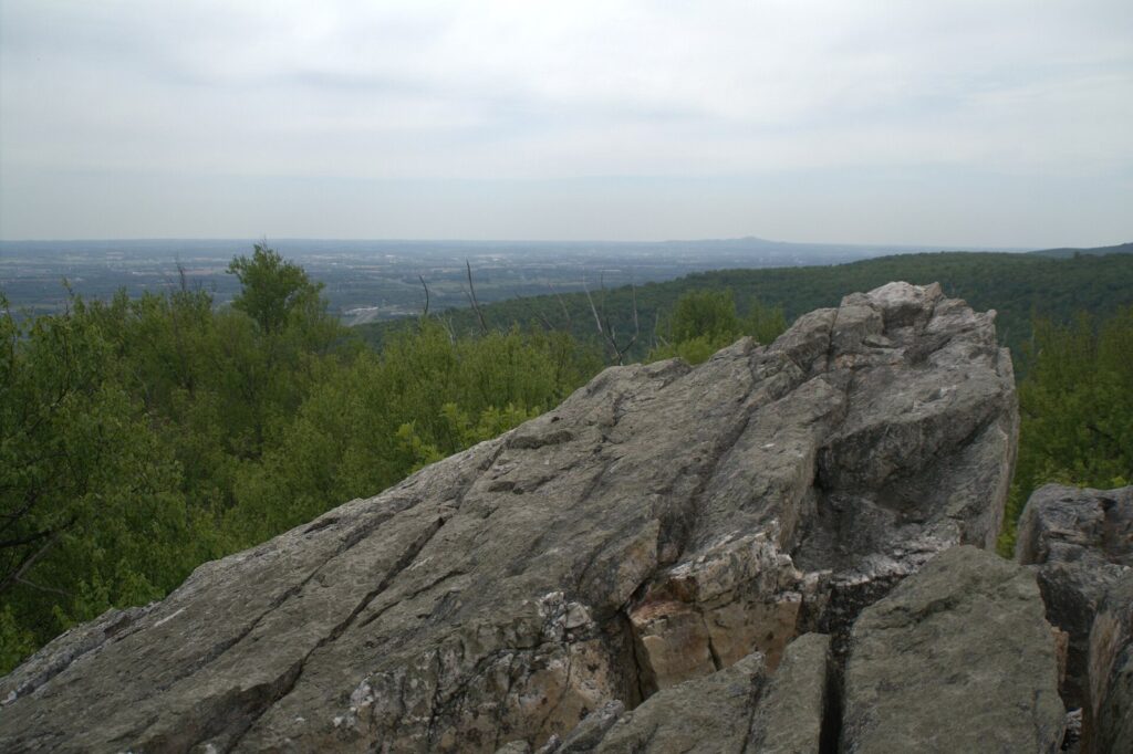 A gray rock outcrop at an overlook above a wooded ridge, with farmland spreading to the horizon