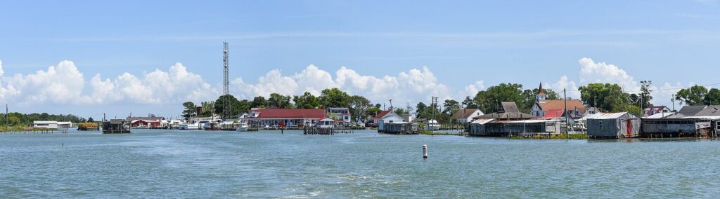 Low white houses, work sheds and docks of Ewell on Smith Island seen across the harbor under summer clouds