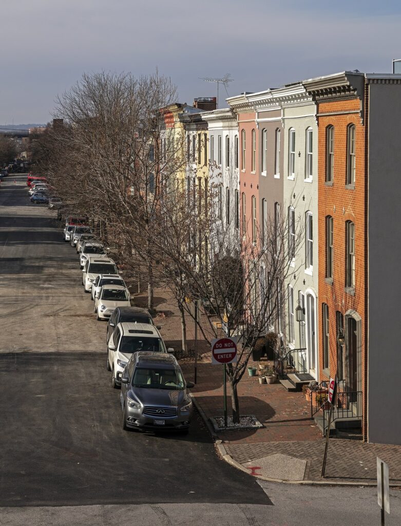 A street of brightly painted brick rowhouses with bare trees and parked cars