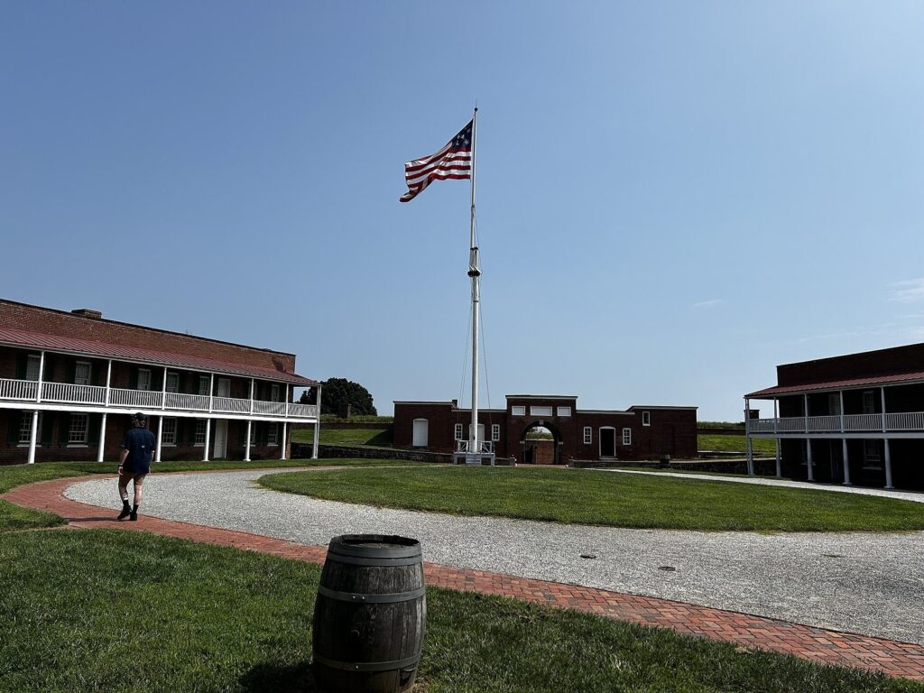 The inside of a star-shaped brick fort with two-story barracks and a flagpole flying the US flag