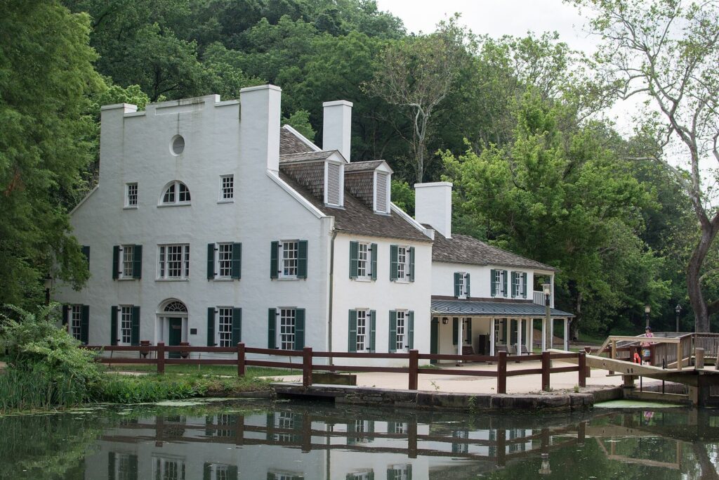 The white Great Falls Tavern with green shutters beside the canal, reflected in the water