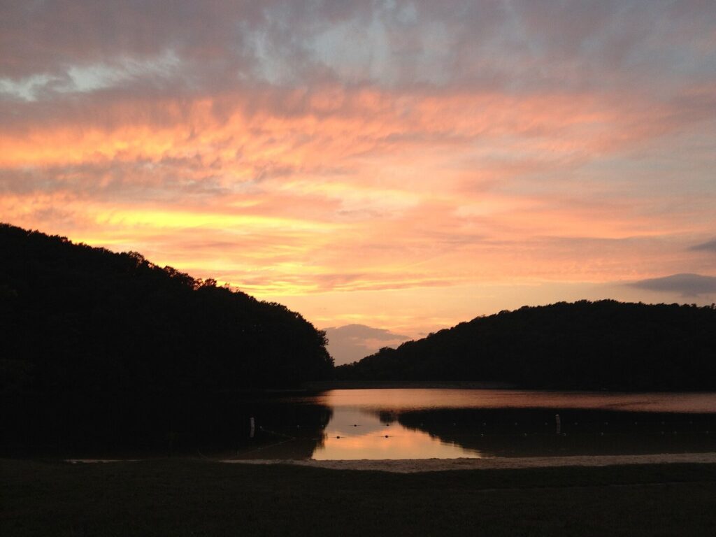 An orange sunset sky over dark wooded hills and the still water of Greenbrier Lake