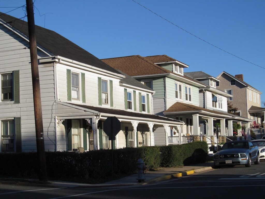A row of two-story clapboard houses with front porches along a residential street