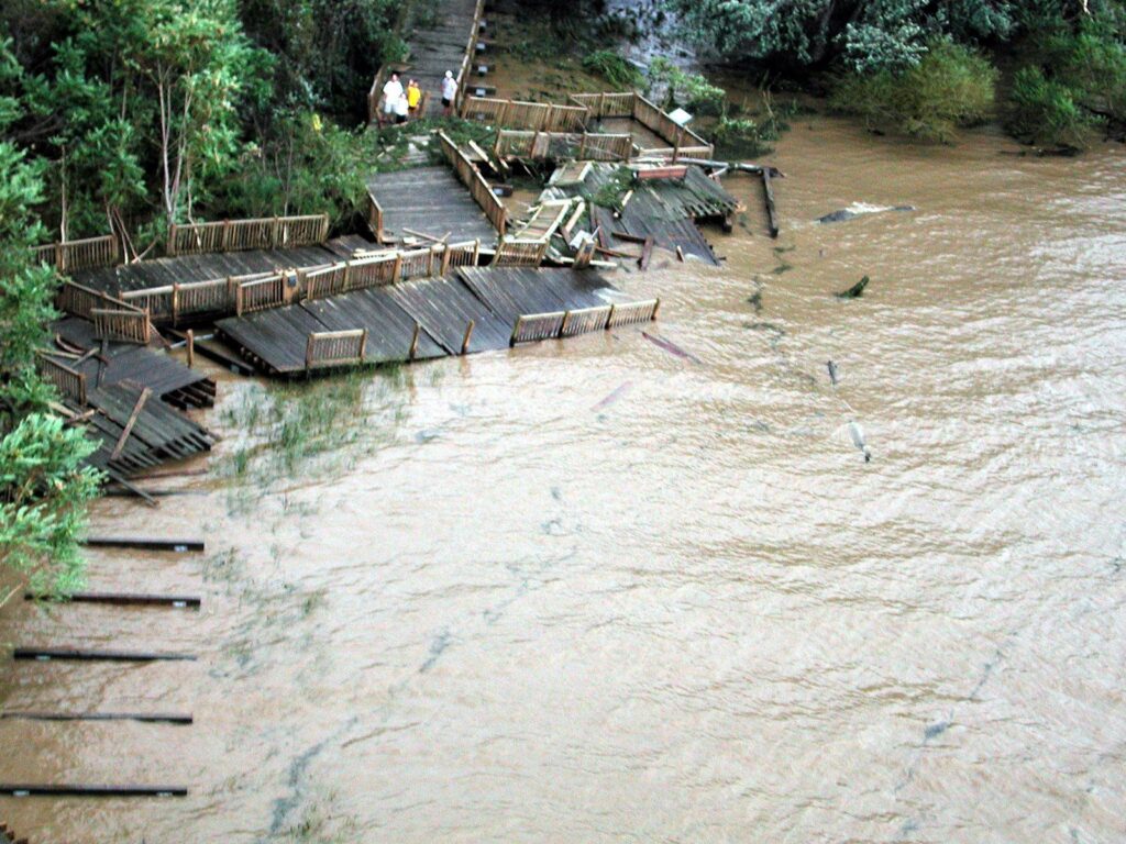 Aerial view of broken boardwalk sections scattered along a muddy, flooded shoreline