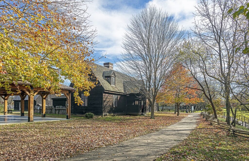 A reconstructed wooden colonial building under autumn trees beside a paved path