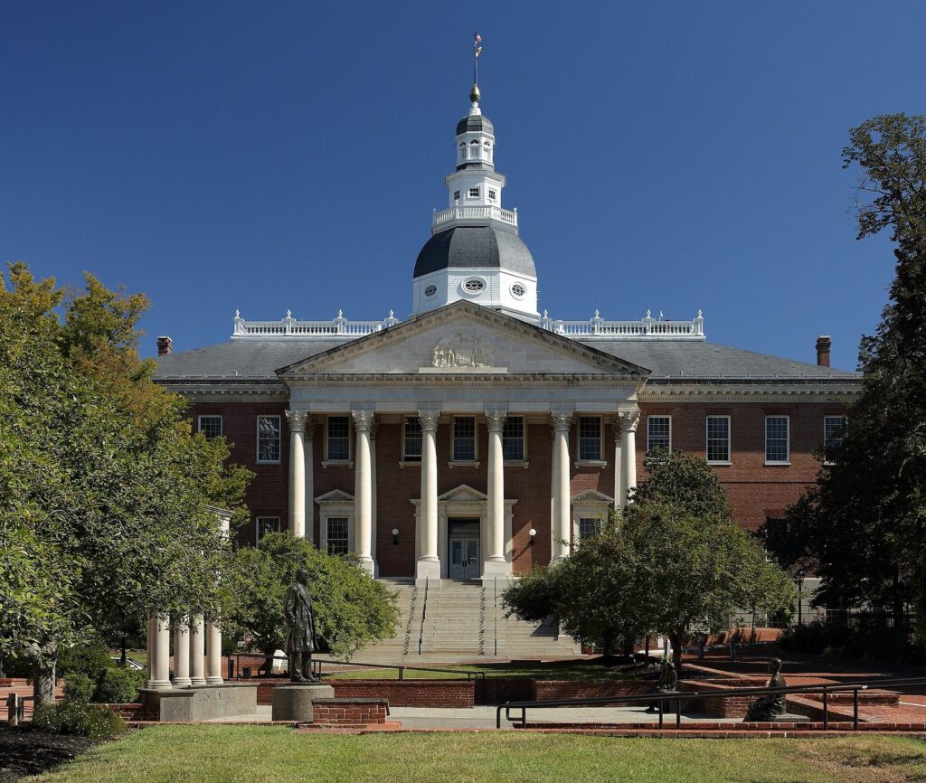 The red-brick State House with its white columned portico and tall white dome under a deep blue sky
