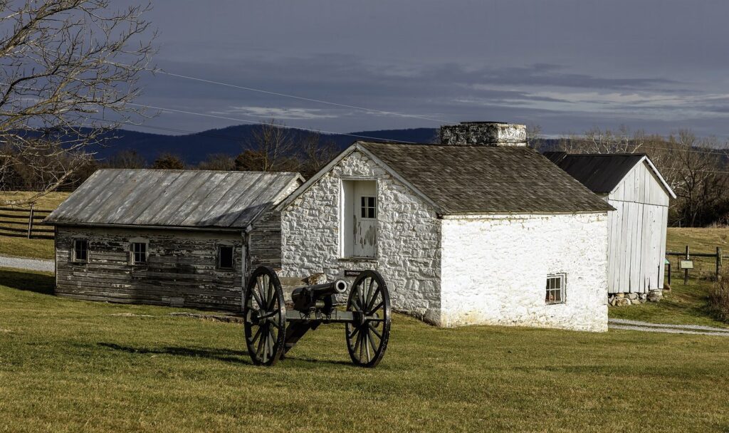 The white stone Mumma farmhouse and outbuildings with a cannon on the lawn and mountains behind
