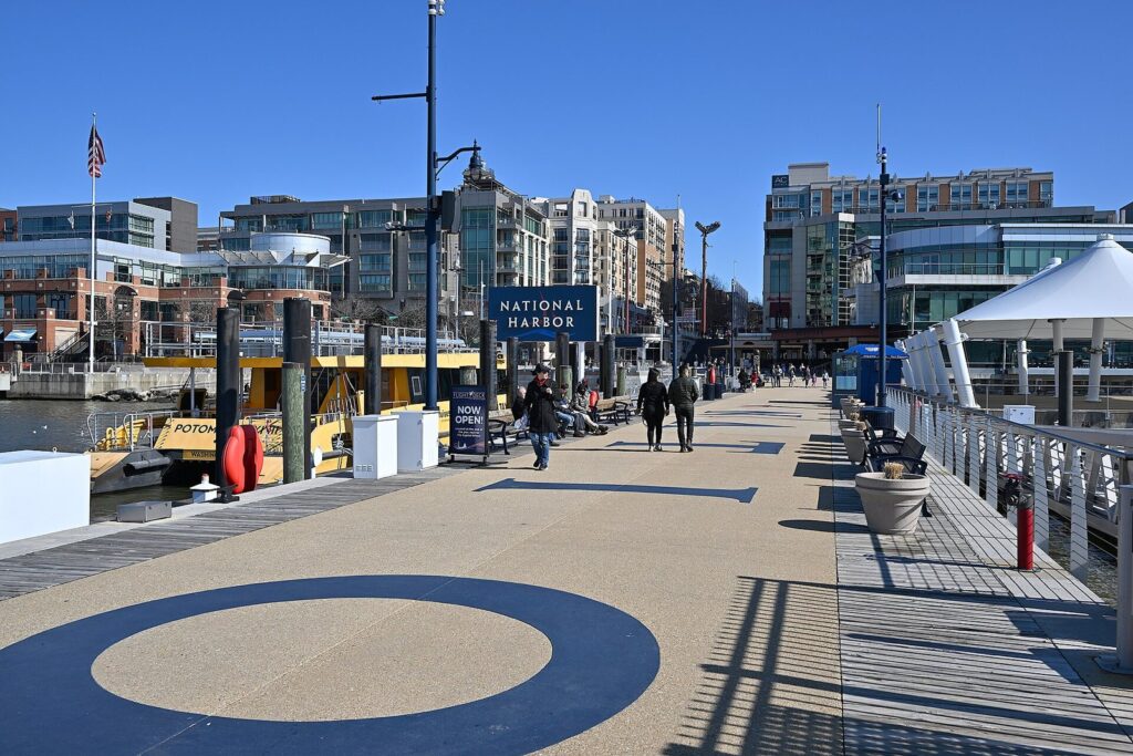 Wide pier with a navy-blue welcome sign, a yellow water taxi tied up alongside and mid-rise hotels behind under a clear sky