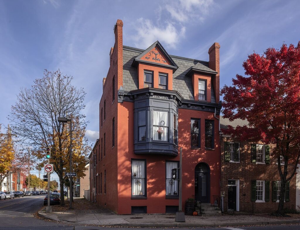 A red-brick Victorian townhouse with a bay window on a corner, framed by red autumn trees