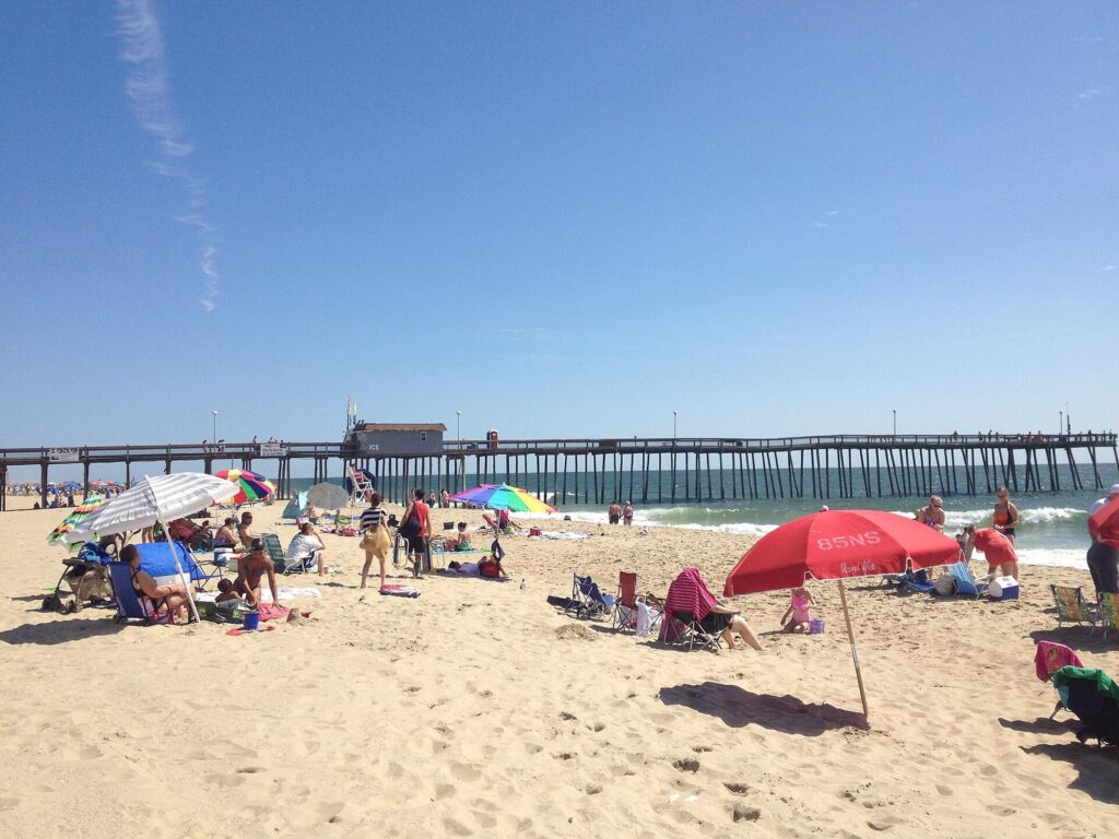Beach umbrellas, chairs and sunbathers on the sand near the fishing pier on a clear summer day