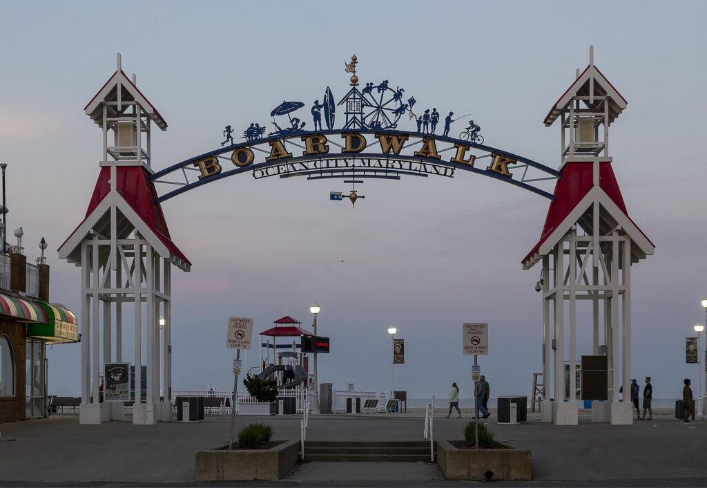 The white Boardwalk arch with red-roofed towers at dusk, with a lifeguard stand and the beach beyond