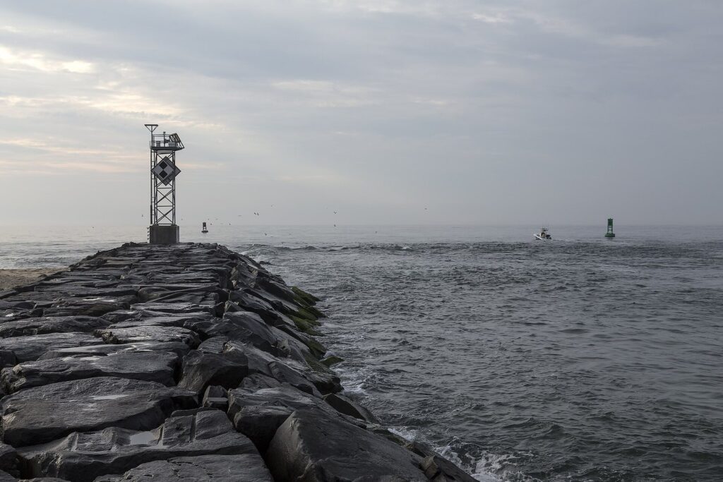 A navigation light tower at the end of the rock jetty at the Inlet, with small boats in the channel