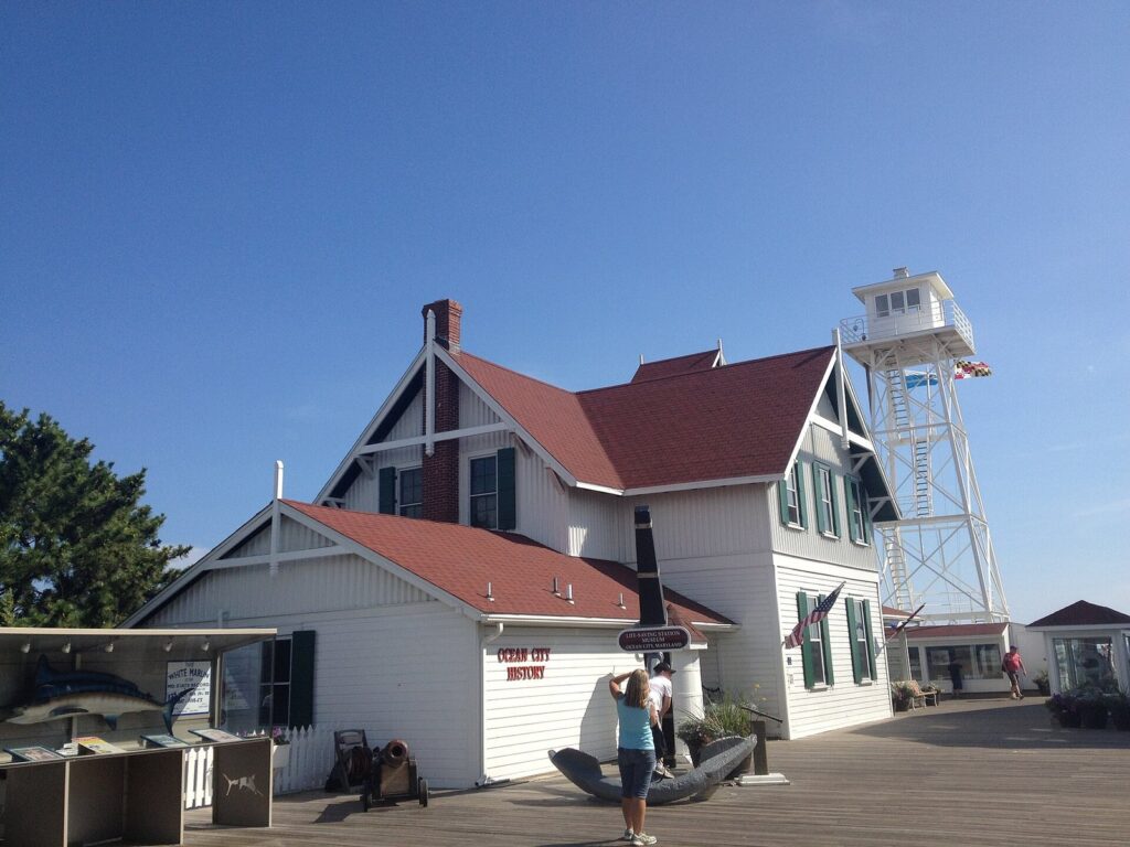 The white Life-Saving Station Museum building with a red roof and a lookout tower, beside the Boardwalk at the Inlet