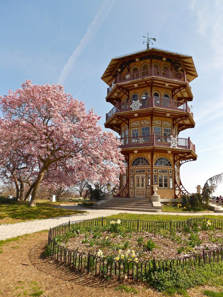 A multi-tiered Victorian pagoda-style observatory tower beside a blooming magnolia in a park
