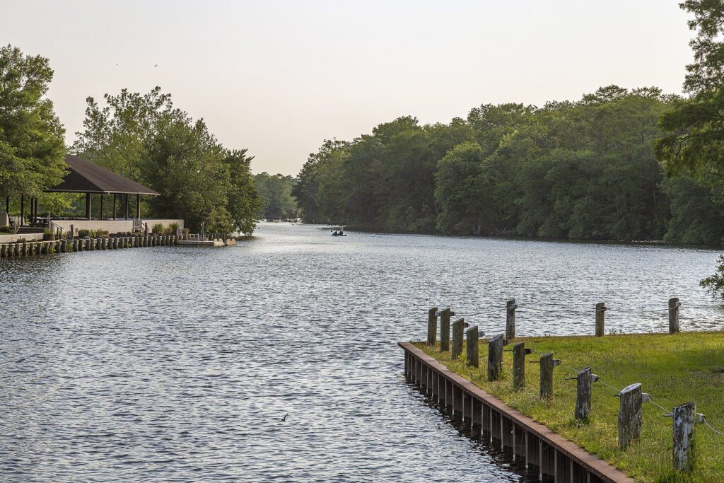 The calm Pocomoke River curving between green woods at Snow Hill, with a wooden bulkhead and a picnic shelter