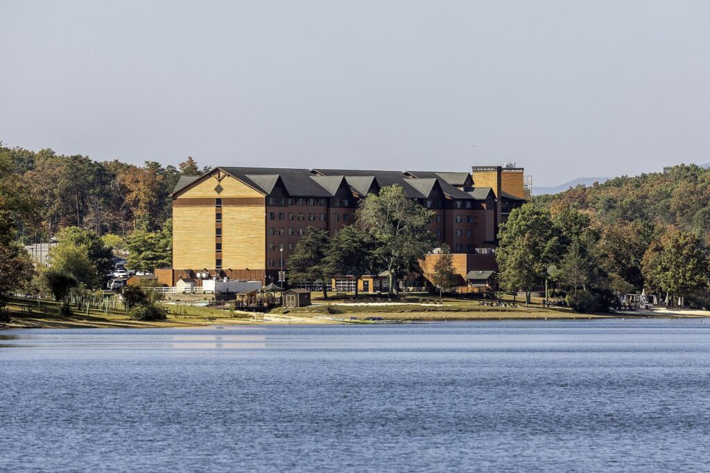 The Rocky Gap resort building across the blue water of Lake Habeeb with early fall color on the hills